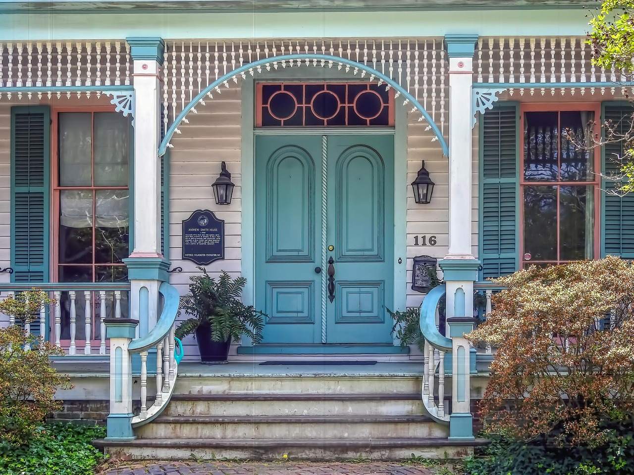 A historic Victorian house with a front porch, teal double doors and a plaque beside the entrance.