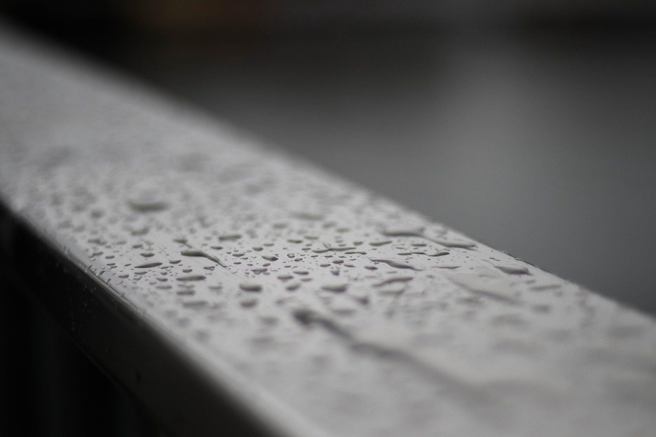 Water droplets on a grey metal gutter edge in front of a blurred background.